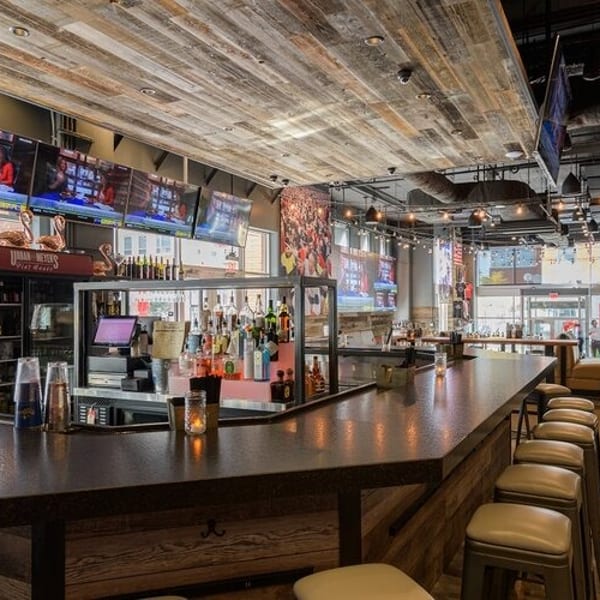 A long, dark wooden bar with stools, multiple TVs, and a rustic wood-paneled ceiling.