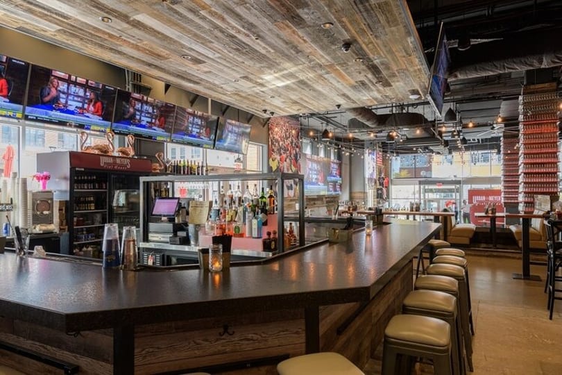 A long, dark wooden bar with stools, multiple TVs, and a rustic wood-paneled ceiling.