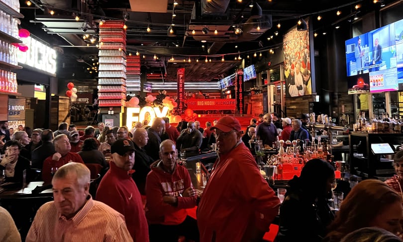 A lively sports bar with many patrons watching a "FOX BIG NOON KICKOFF" event on large screens.
