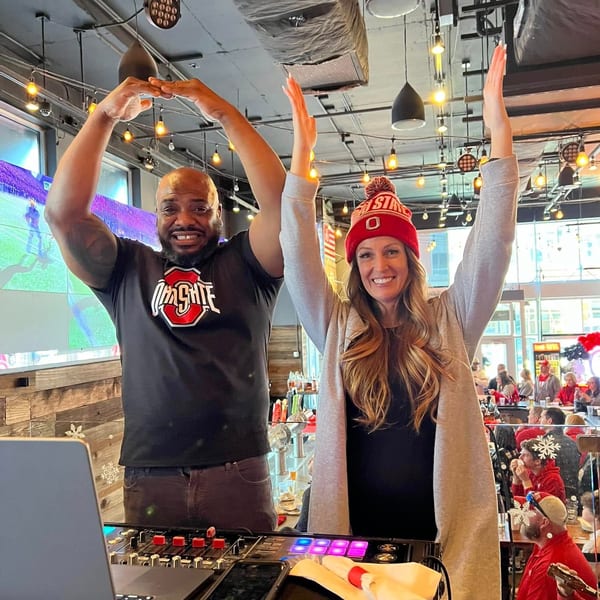Two people, a man and a woman, making an "O" with their arms in a lively restaurant.