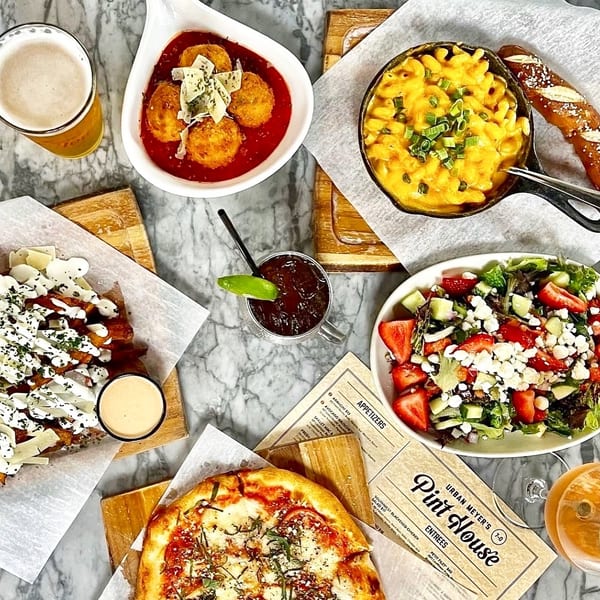 Overhead view of various dishes including pizza, mac and cheese, salad, fries, and drinks on a marble table.