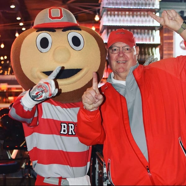 Brutus Buckeye mascot and a man in a red jacket and hat pose with thumbs up.
