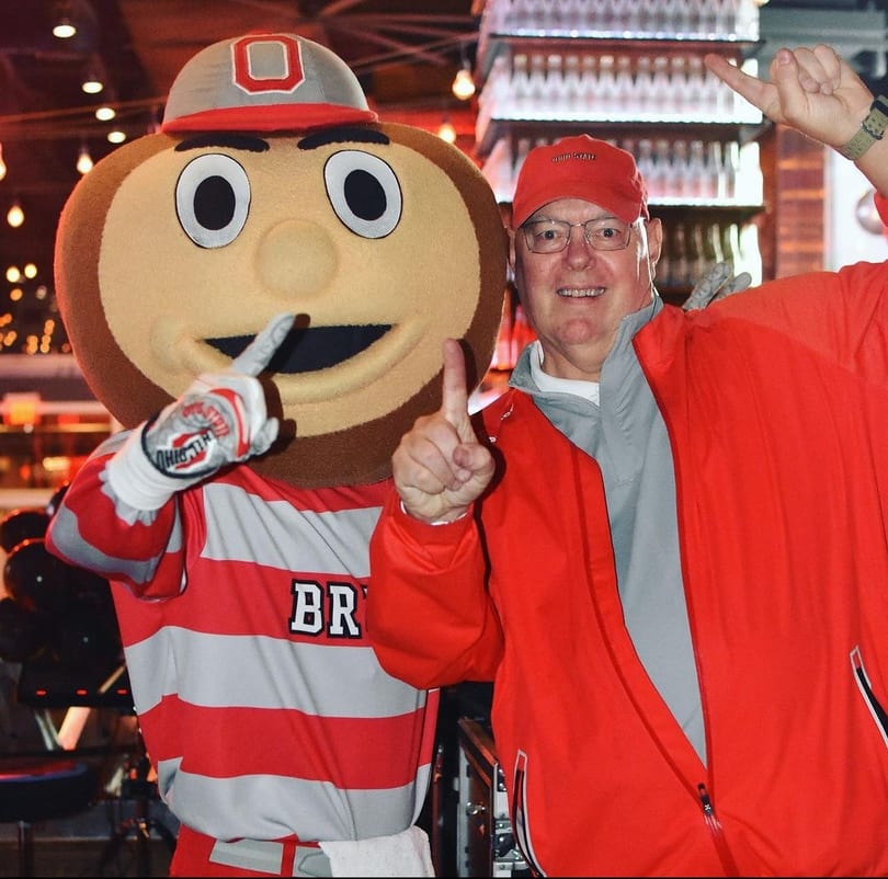 Brutus Buckeye mascot and a man in a red jacket and hat pose with thumbs up.