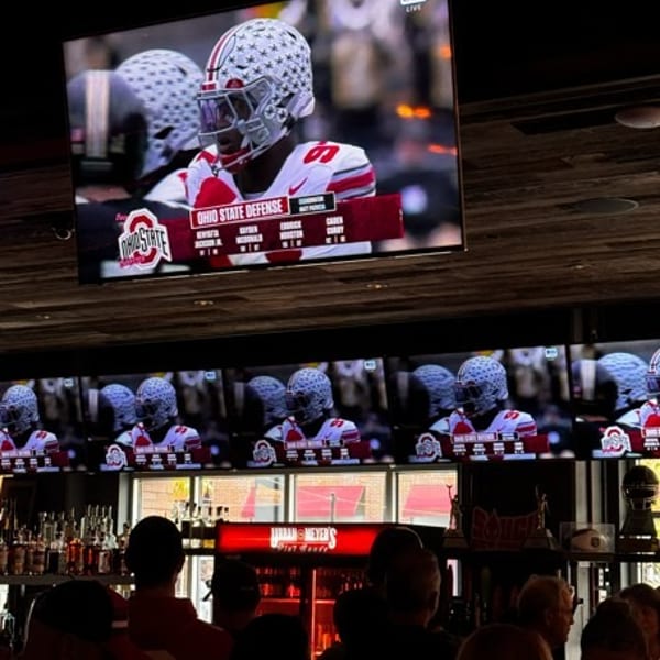 Patrons watch a football game on multiple screens above a bar, with bottles and glasses visible.