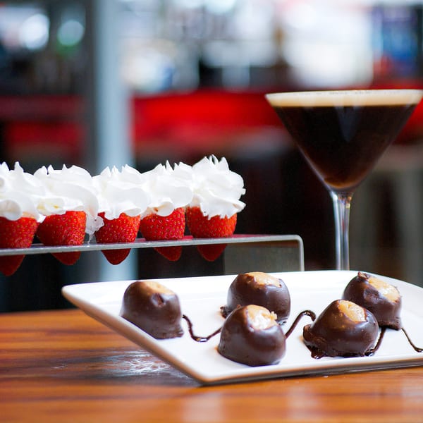 Strawberries with whipped cream, chocolate-covered peanut butter balls, and a martini on a wooden table.