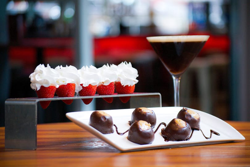 Strawberries with whipped cream, chocolate-covered peanut butter balls, and a martini on a wooden table.