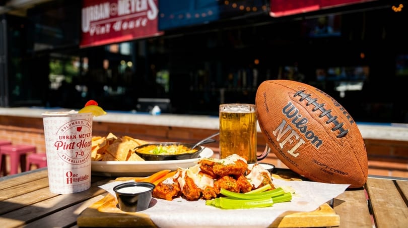 Wings, nachos, beer, and a football on a wooden table at Urban Meyer's Pint House.