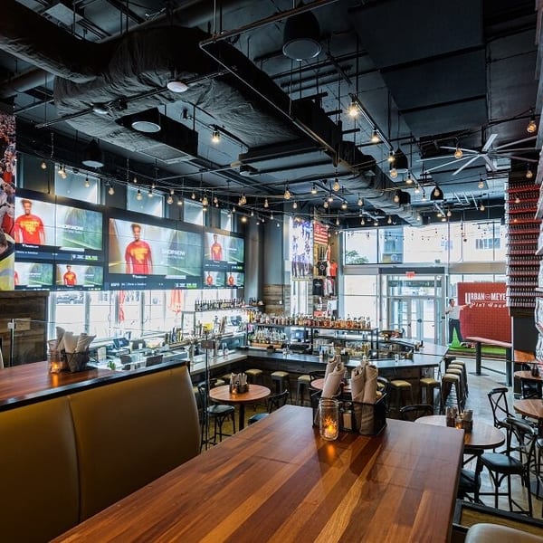 A sports bar interior with large TVs, a long bar, wooden tables, and booths.