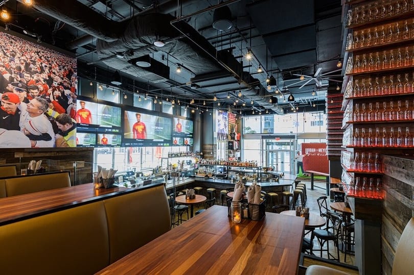 A sports bar interior with large TVs, a long bar, wooden tables, and booths.