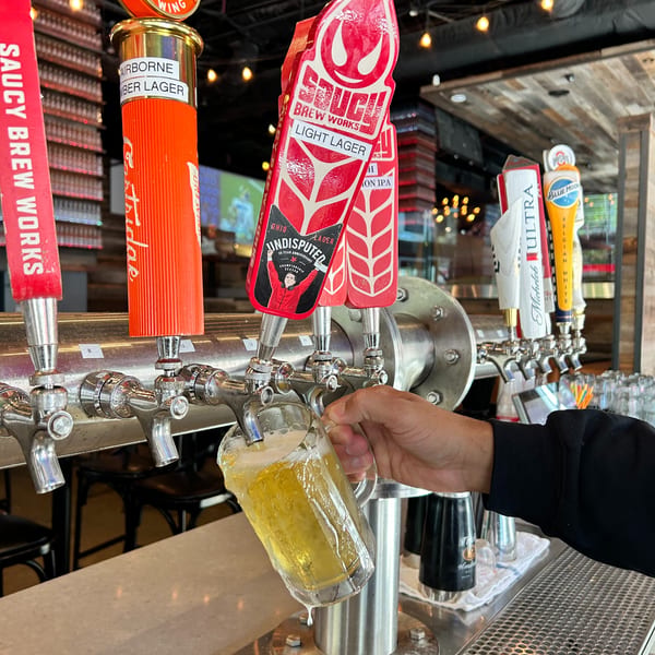 A hand fills a glass with beer from a tap, with several other beer taps visible.