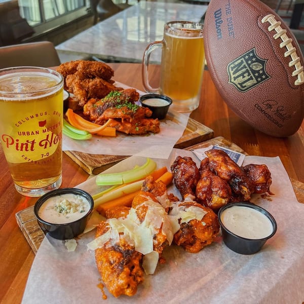 Urban Meyer's Pint House beer glasses, various chicken wings, and an NFL football on a wooden table.