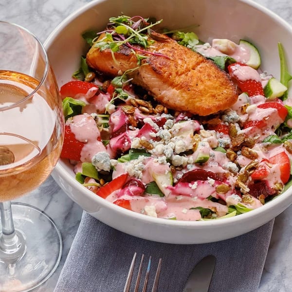 Salmon salad with strawberries, blue cheese, nuts, and pink dressing, next to a glass of rosé.