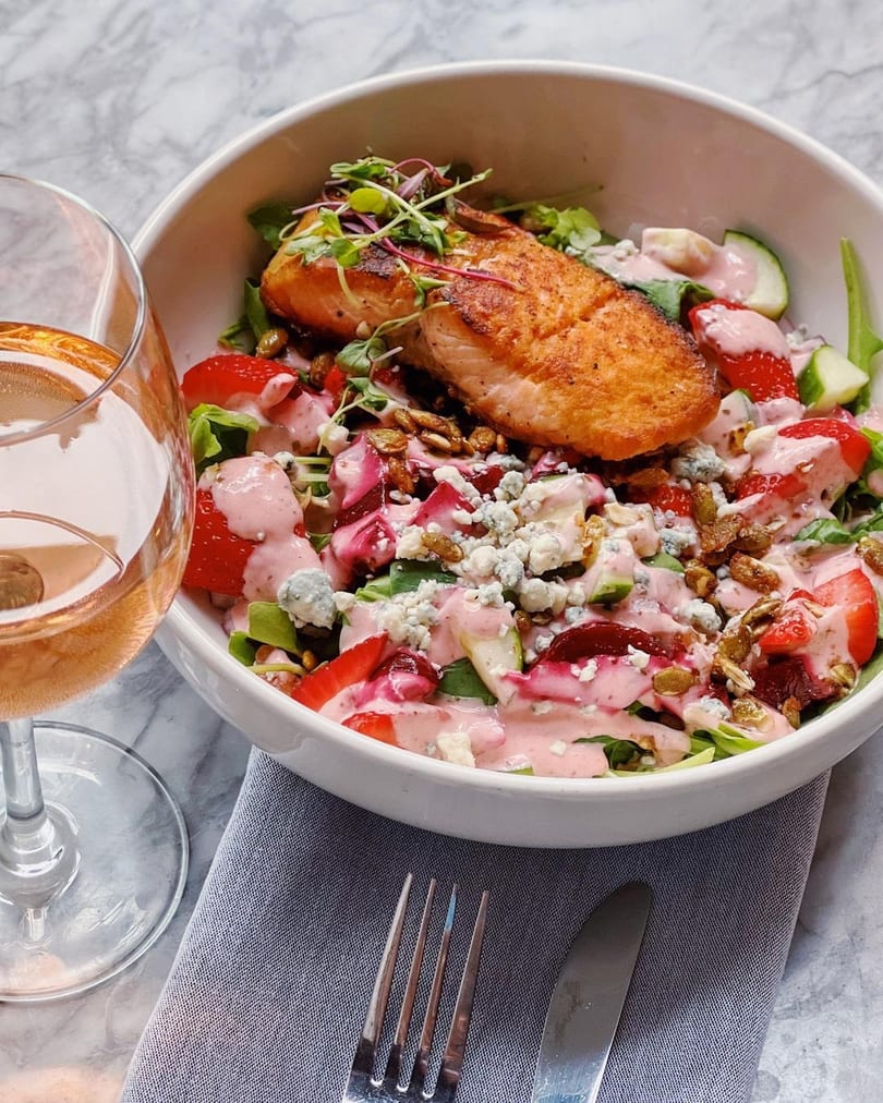Salmon salad with strawberries, blue cheese, nuts, and pink dressing, next to a glass of rosé.