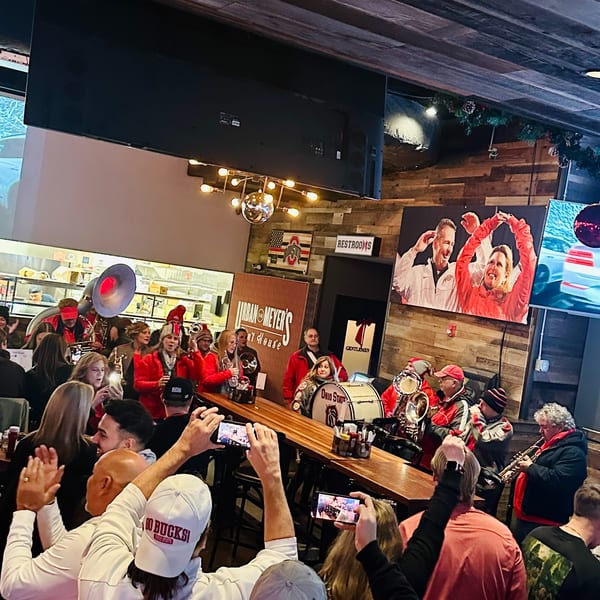 A band in red uniforms plays instruments for a crowd at Urban Meyer's Pint House.