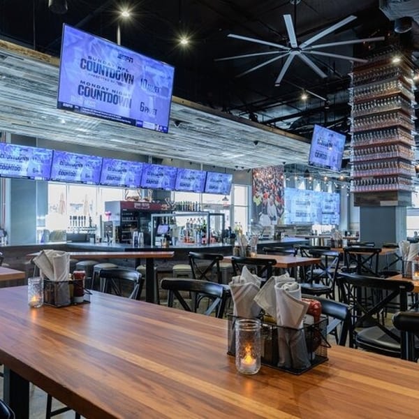 Spacious sports bar interior with multiple large screens, wooden tables, and a long bar area.