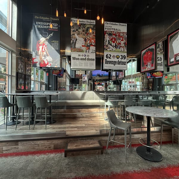 Interior of a sports bar with high-top tables, bar stools, and large sports-themed newspaper clippings.