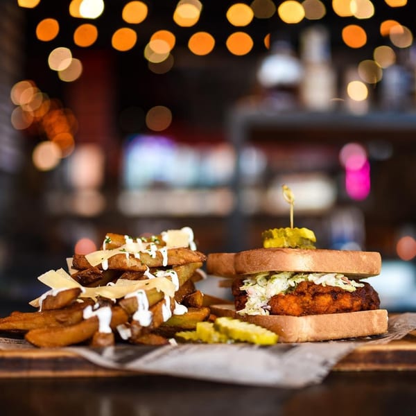 A fried chicken sandwich with coleslaw and pickles, alongside a pile of loaded fries.