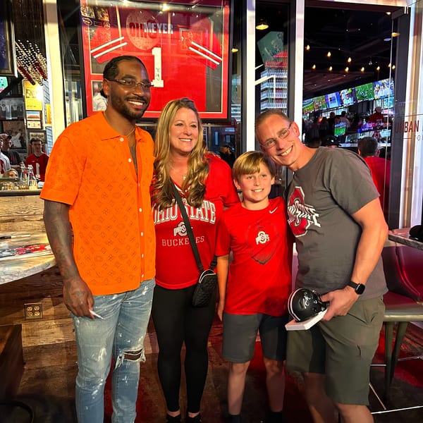 A man in an orange shirt poses with a family of three, all smiling in a restaurant.