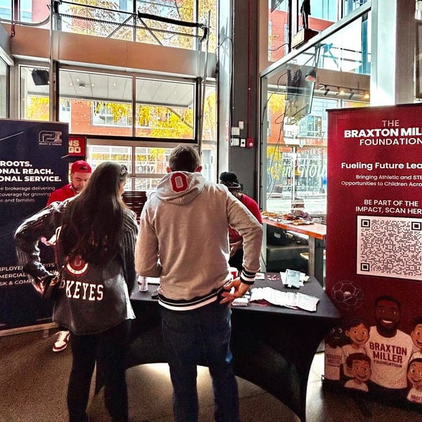 People gather around tables with promotional banners for Ohio Roots and The Braxton Miller Foundation.